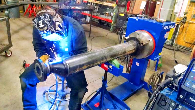 A man is welding a pipe in a factory.