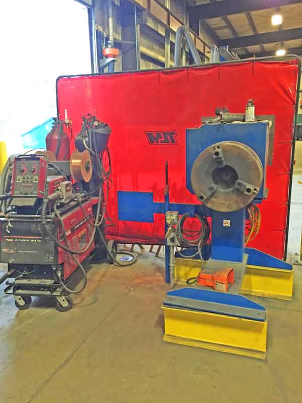A welding machine is sitting in front of a red wall that says vox