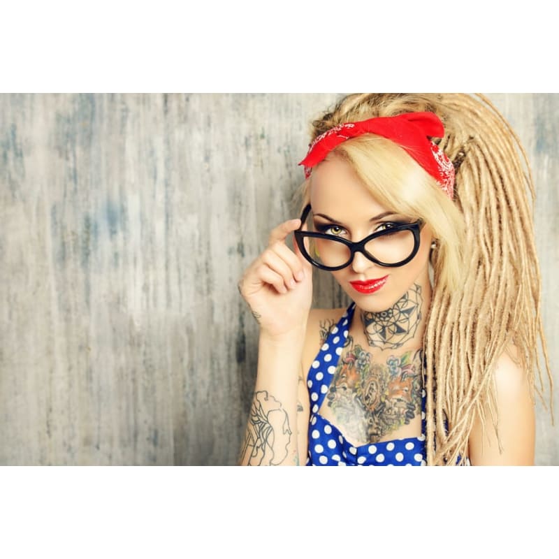 A woman with dreadlocks and tattoos is wearing glasses and a bandana.