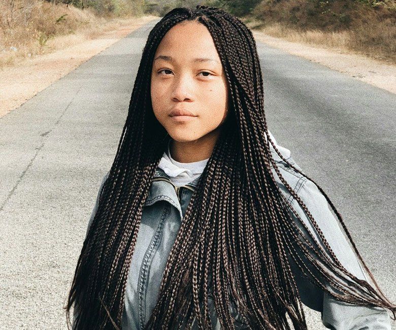 A young girl with braids is standing on the side of a road.