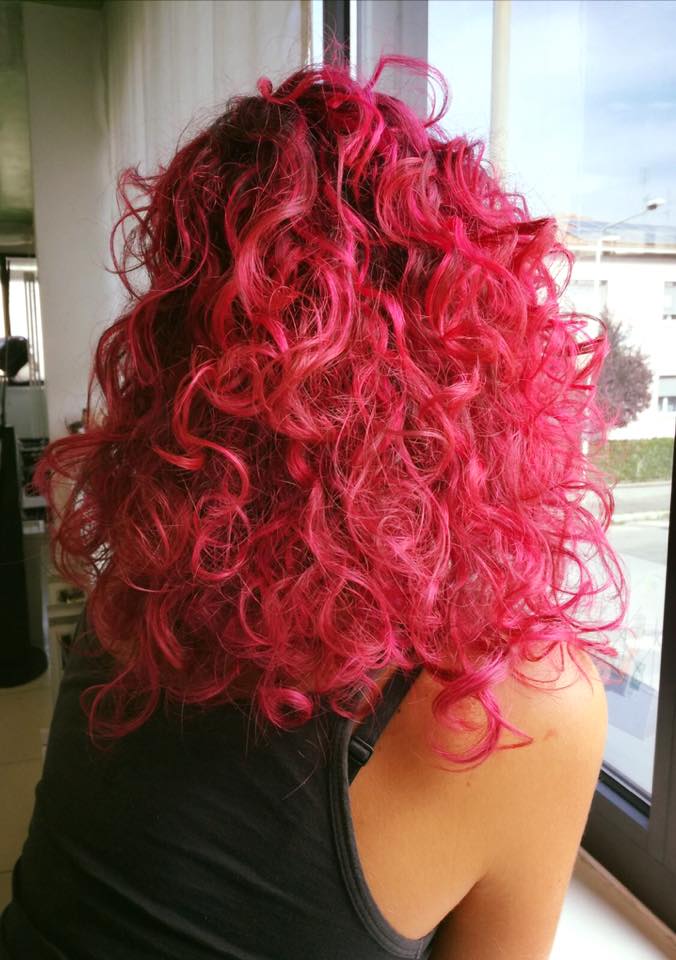 Donna con i capelli ricci e rosa acceso, che guarda fuori dalla finestra.
