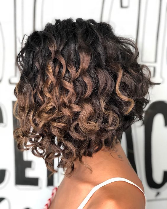 Donna con capelli scuri e ricci, raccolti in un caschetto scalato con riflessi castani.