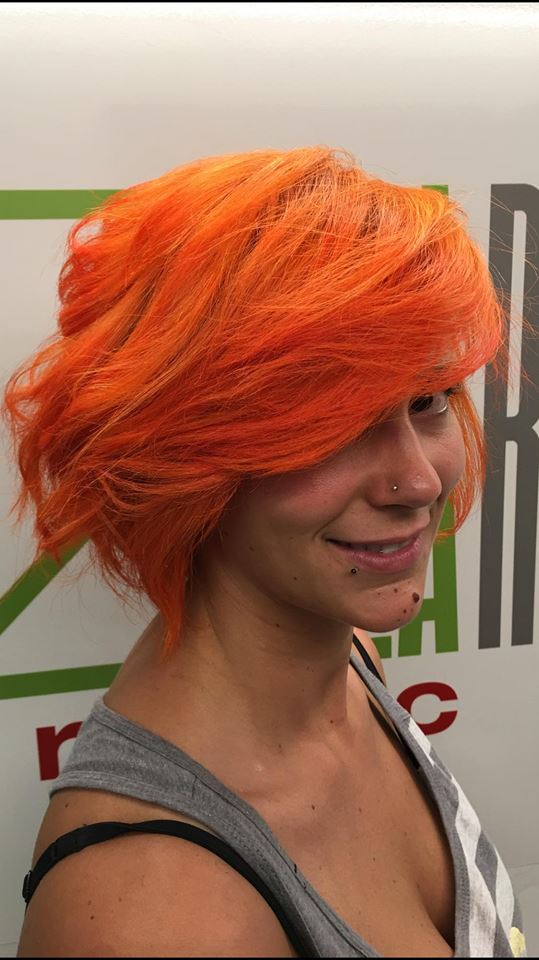 Donna con capelli corti, di un arancione brillante, che sorride leggermente.