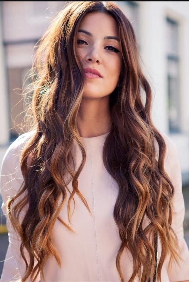 Donna con lunghi capelli castani ondulati con riflessi biondi, che indossa un top rosa chiaro, all'aperto.