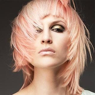 Donna con capelli color pesca scalati, trucco scuro sugli occhi e un'espressione seria.