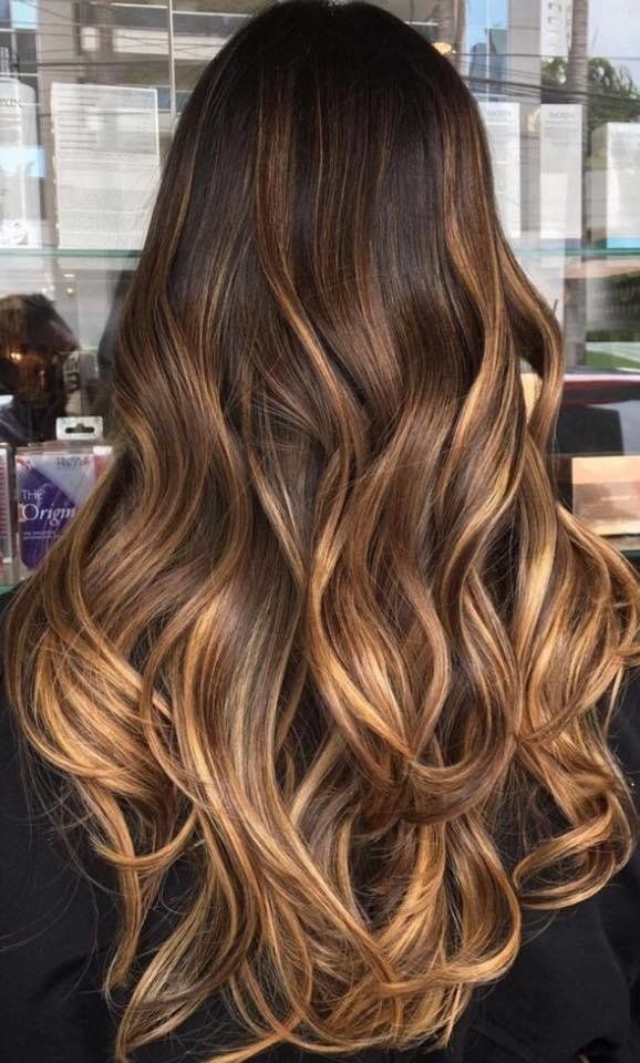 Capelli ondulati da donna con radici castano scuro che sfumano in riflessi biondo caramello e dorato.