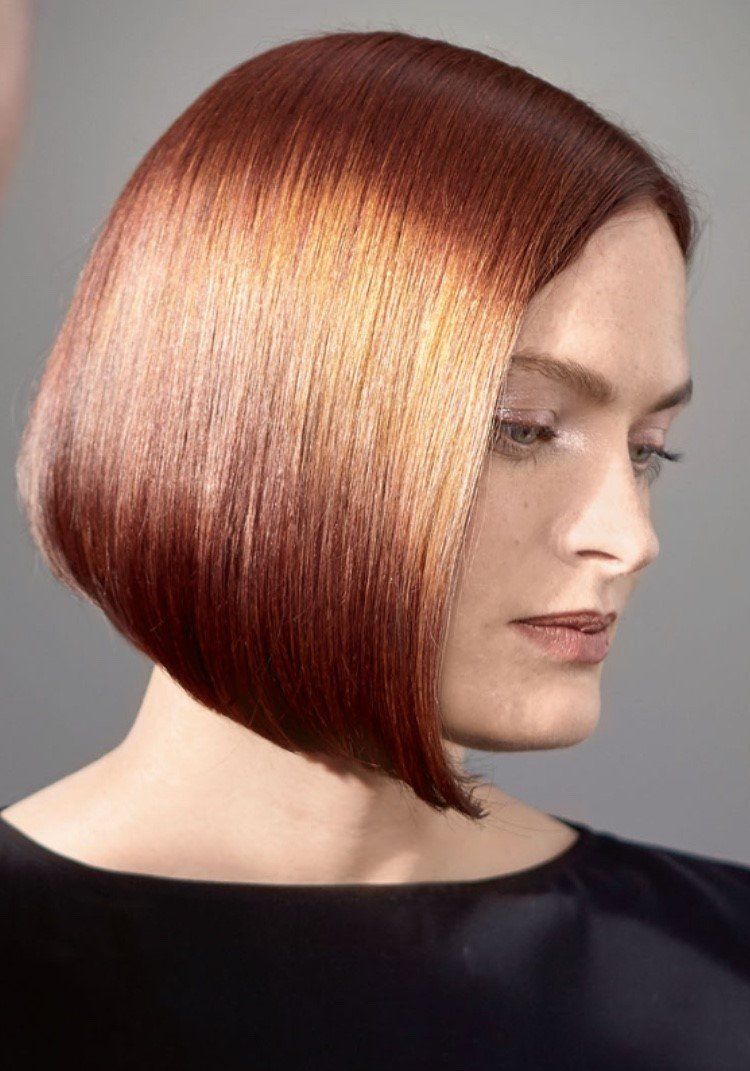 Donna con taglio di capelli castano ramato liscio e angolato, illuminato da mèches luminose.