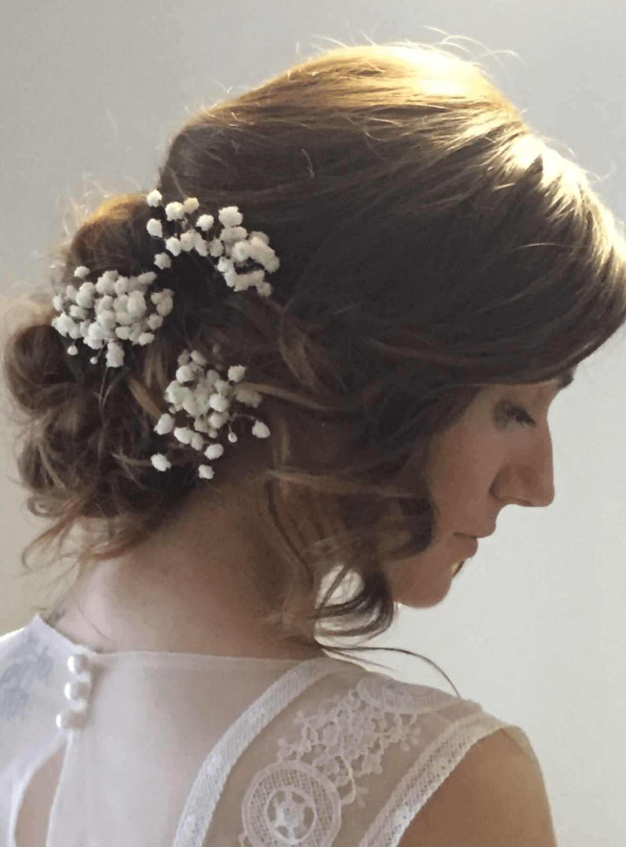 Donna con abito bianco e acconciatura raccolta decorata con fiori di gypsophila.