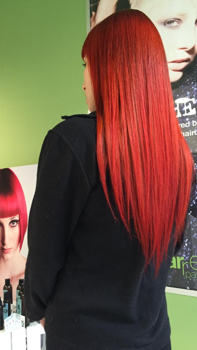 Persona con lunghi capelli rossi e lisci, che indossa un top nero, in un salone di bellezza.
