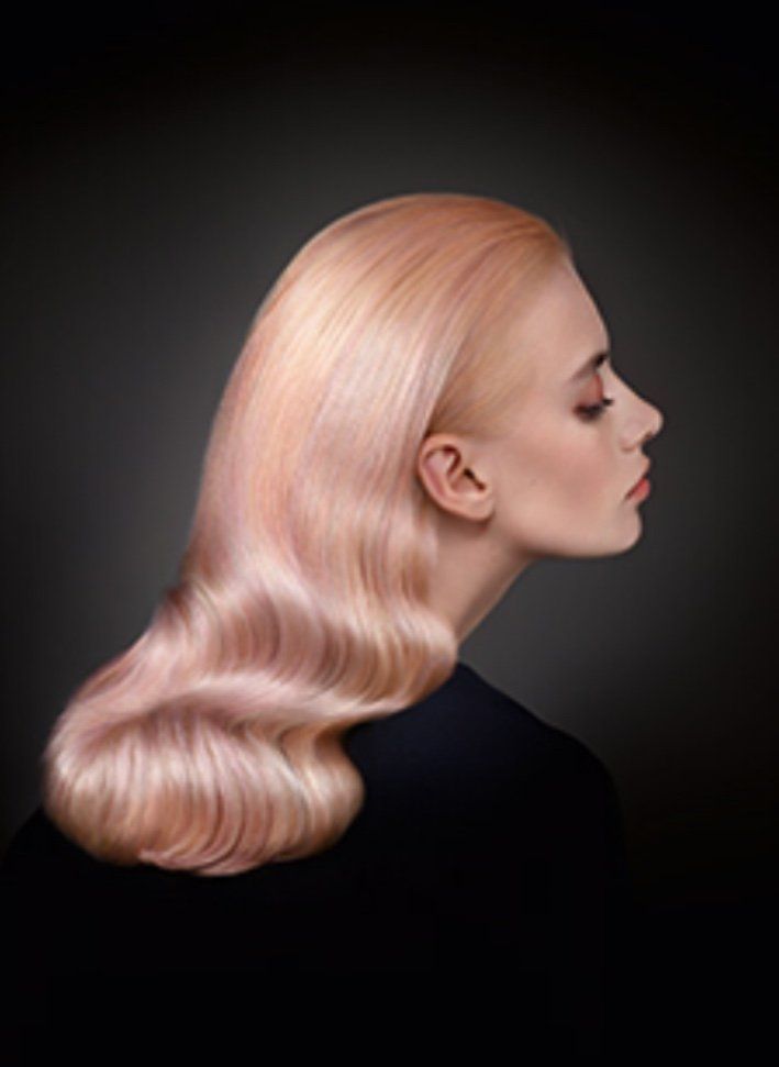 Donna con capelli ondulati color pesca, vista di profilo, sfondo scuro, vestita di nero.