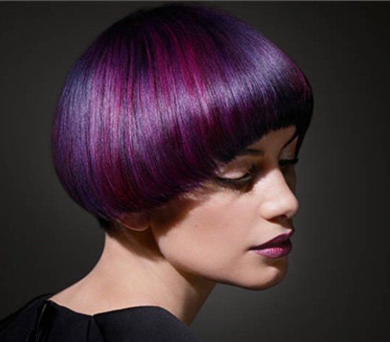 Donna con capelli corti, rotondi, viola e magenta. Sfondo scuro.