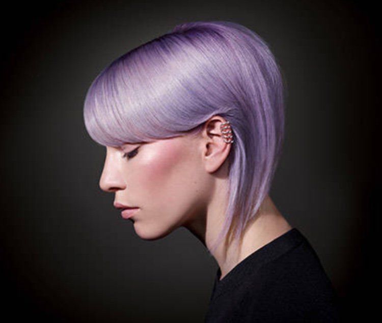 Donna con capelli corti color lavanda, caschetto angolato, sfondo scuro, vestita di nero.