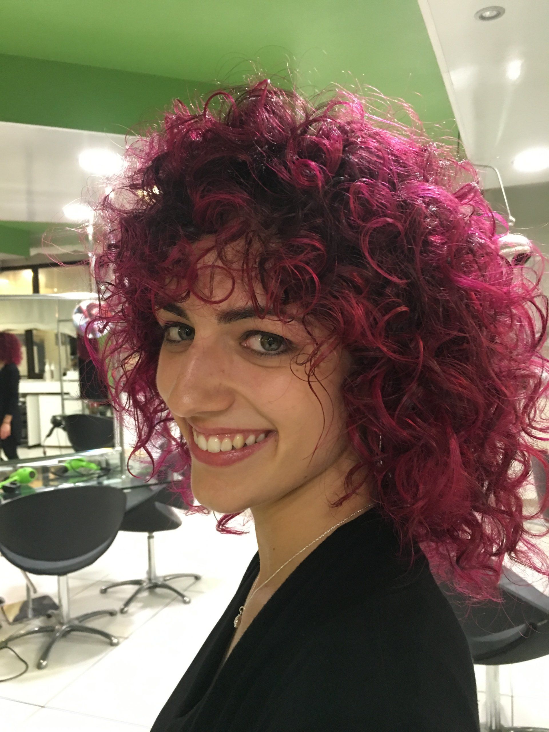 Una donna con i capelli ricci rosa acceso sorride in un salone di bellezza.