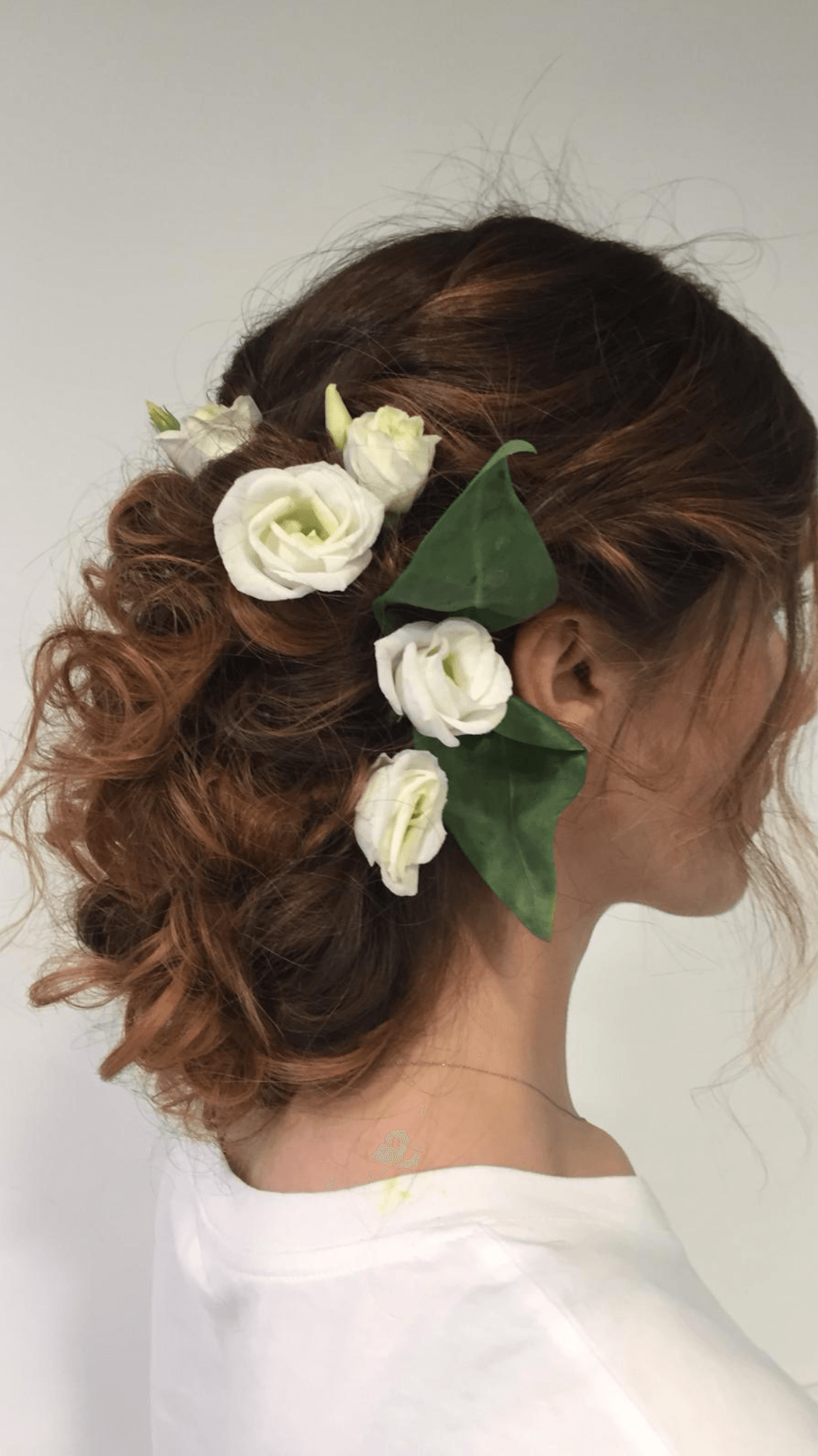 Donna con i capelli castani raccolti in uno chignon, decorato con fiori bianchi e foglie verdi.
