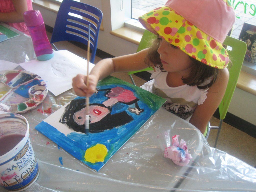 A little girl wearing a pink hat is painting a picture