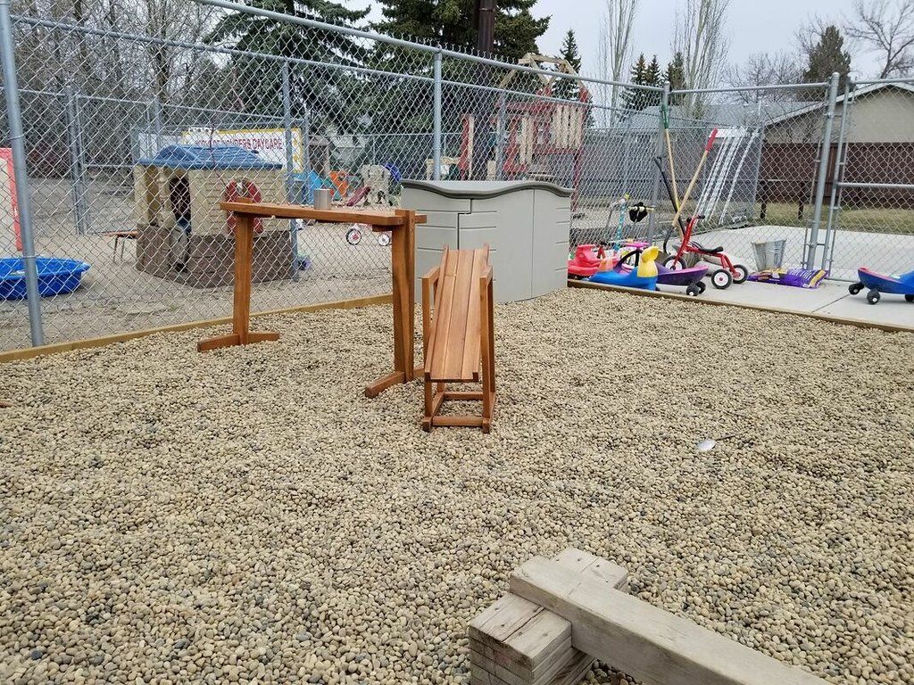 A wooden table is sitting in the middle of a gravel playground.
