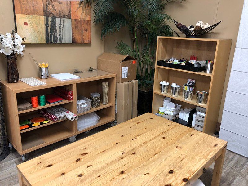 A room with a wooden table , shelves , and a painting on the wall.
