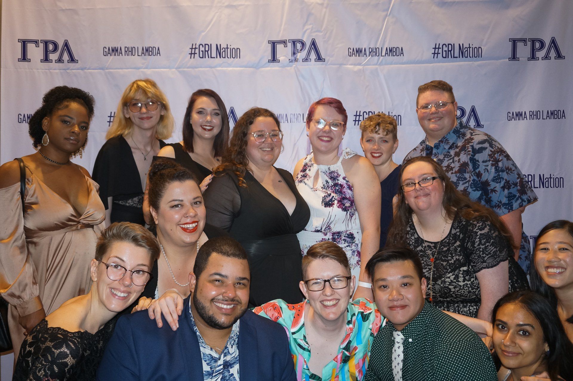 A large group of people, nicely dressed, stand in front of a background with text on it.