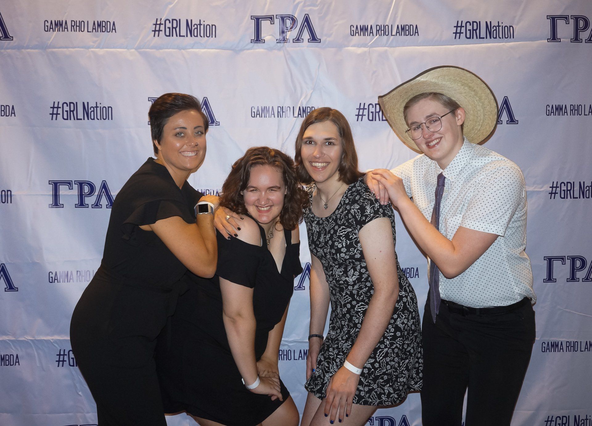 Four people, nicely dressed, stand in front of a background with text on it.