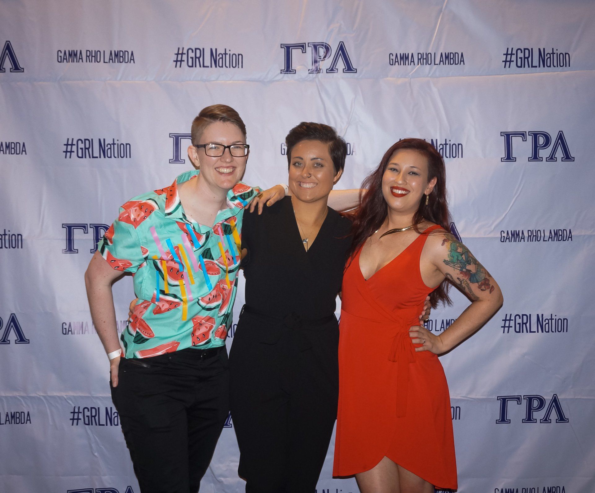 Three people, nicely dressed, stand in front of a background with text on it.