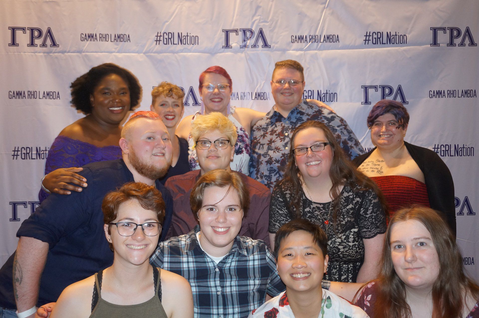 A large group of people, nicely dressed, stand in front of a background with text on it.
