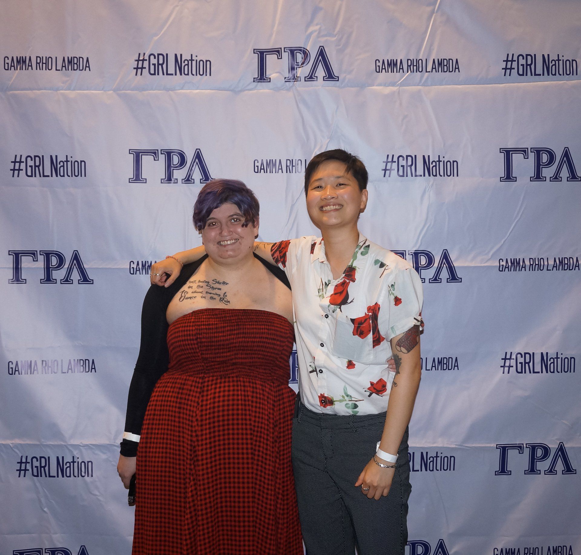 Two people, nicely dressed, stand in front of a background with text on it.