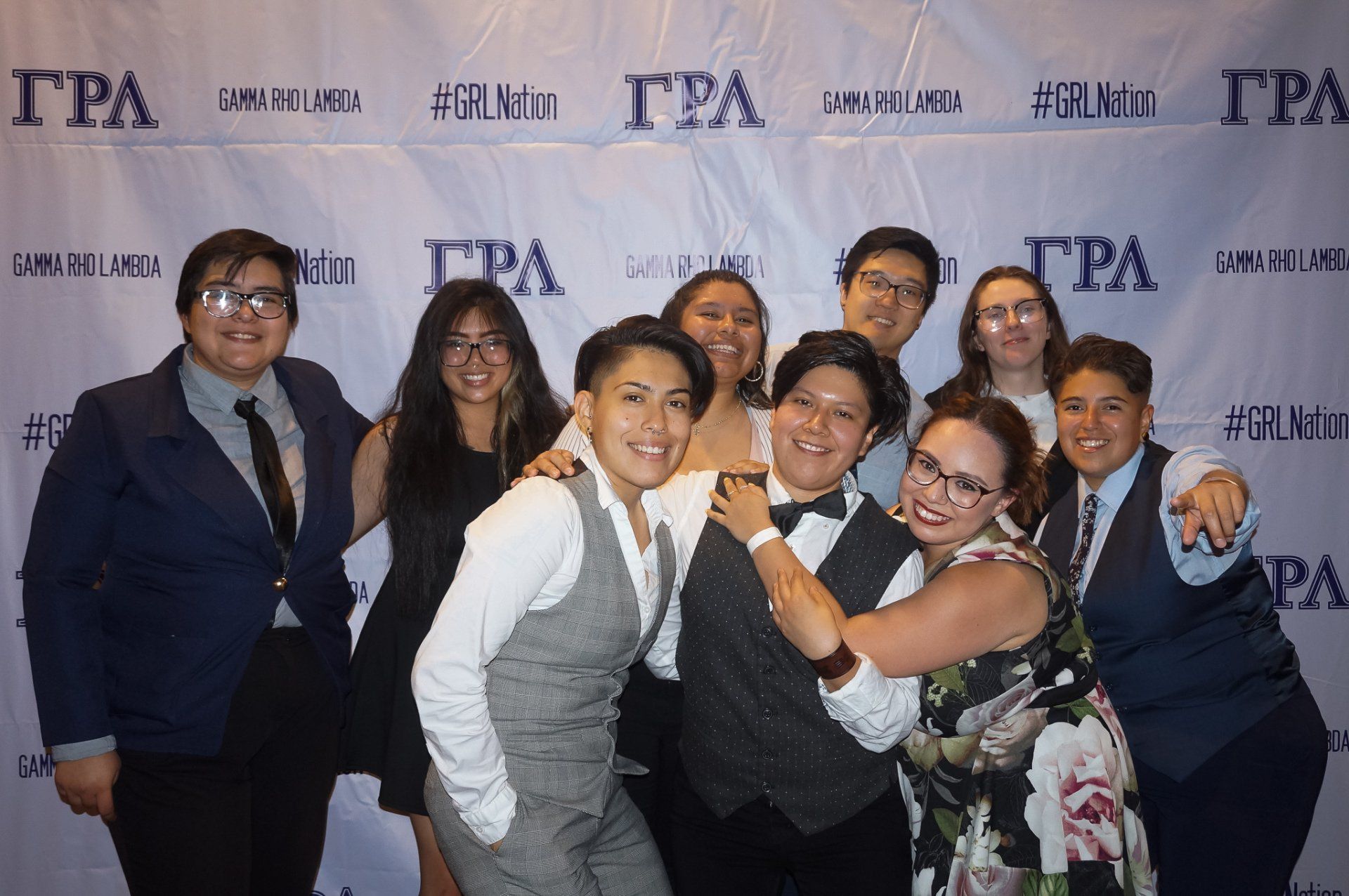 A large group of people dress in formal attire pose in front of a background with text on it.