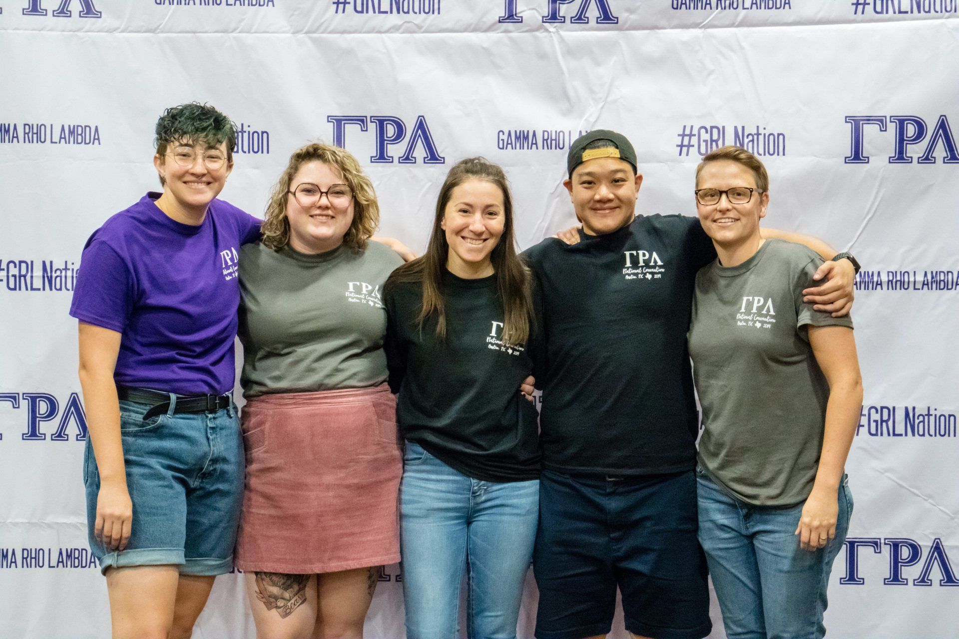 A group of 5 people pose together in front of a background with text.