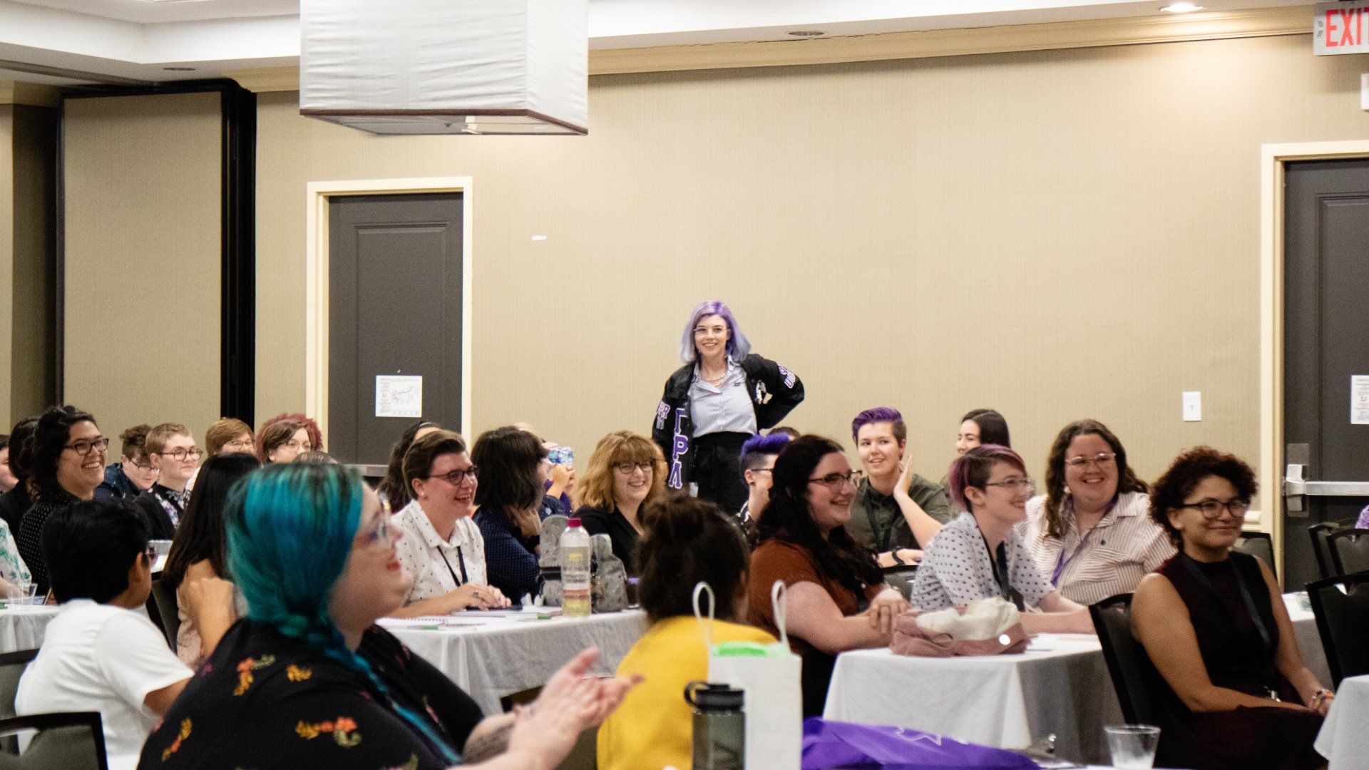 A group of people sitting at a coference, listening to a person in the group who is speaking