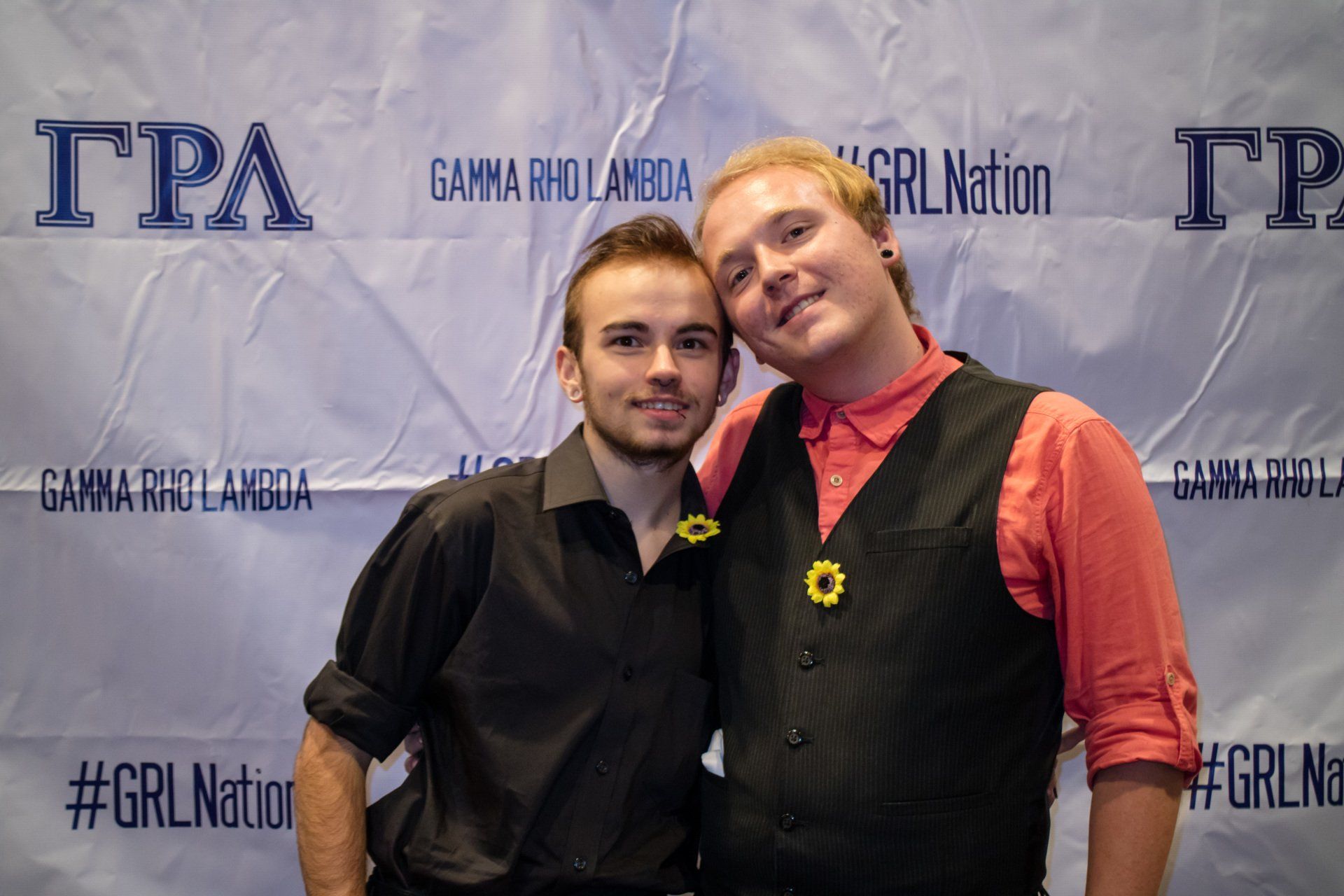 Two people, nicely dressed, stand in front of a background with text on it.