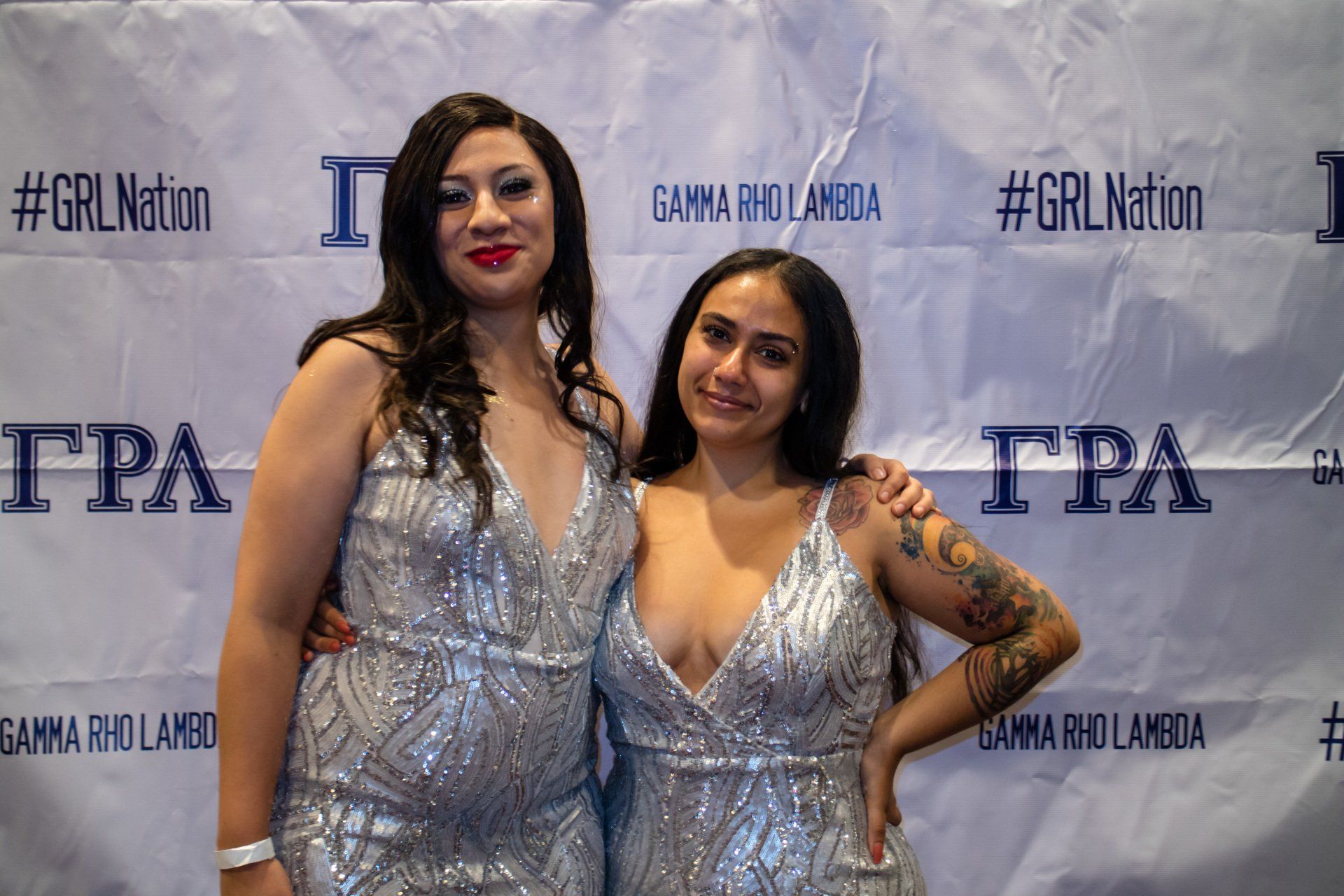 Two people, nicely dressed, stand in front of a background with text on it.