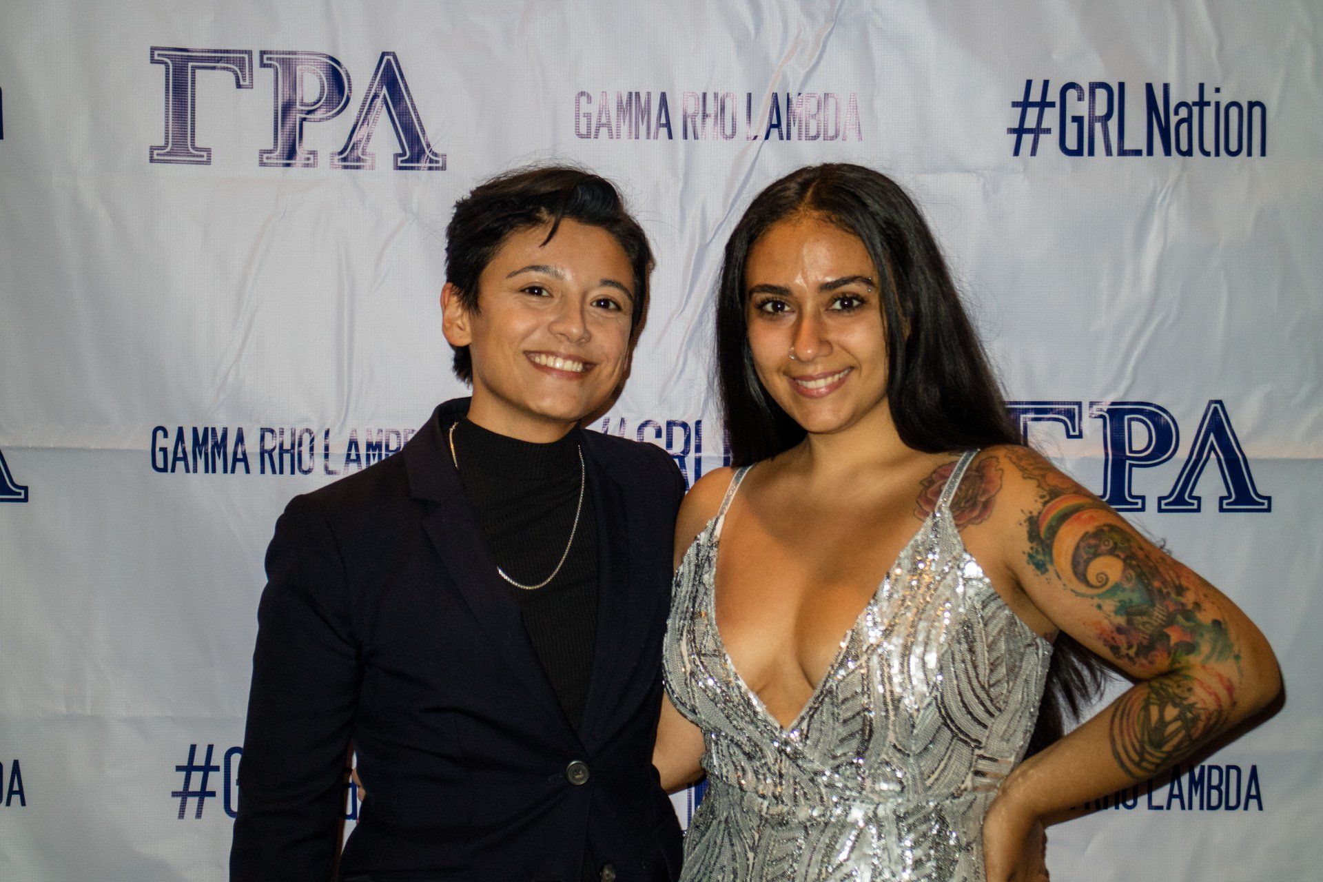 Two people, nicely dressed, stand in front of a background with text on it.