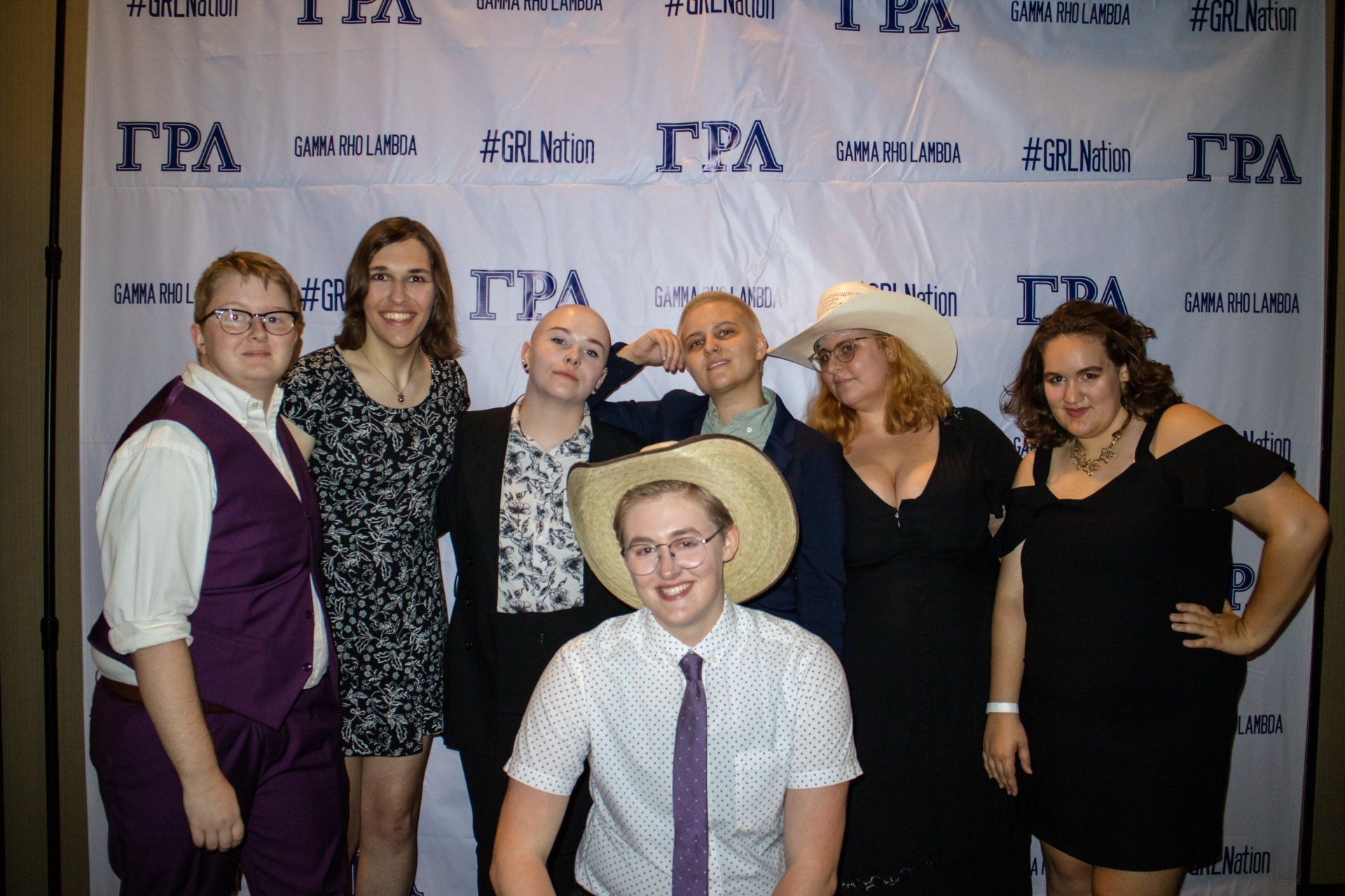 A large group of people dress in formal attire pose in front of a background with text on it.