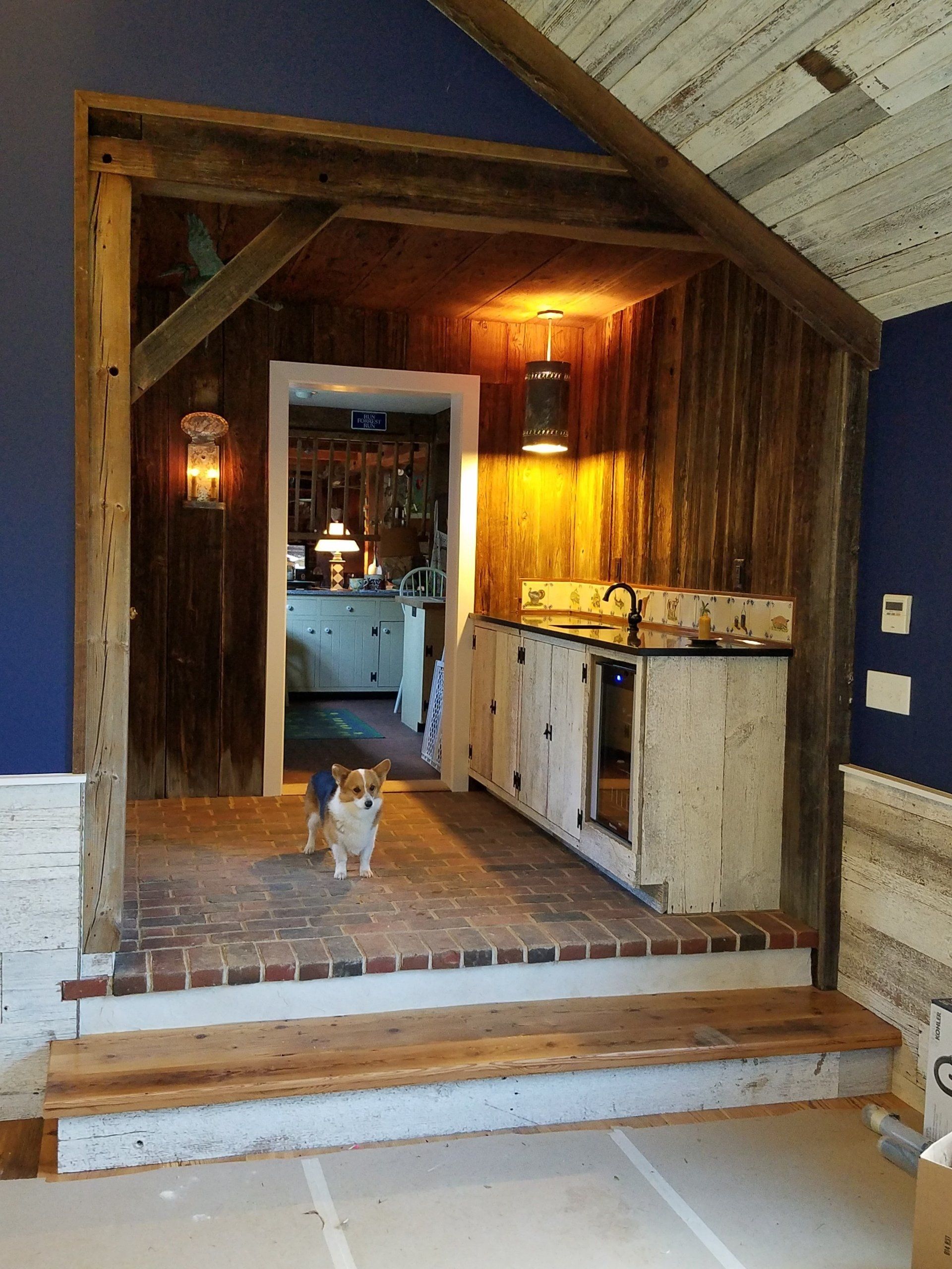 Rustic wooden bar area with brick floor, small dog, and a glimpse of a kitchen.