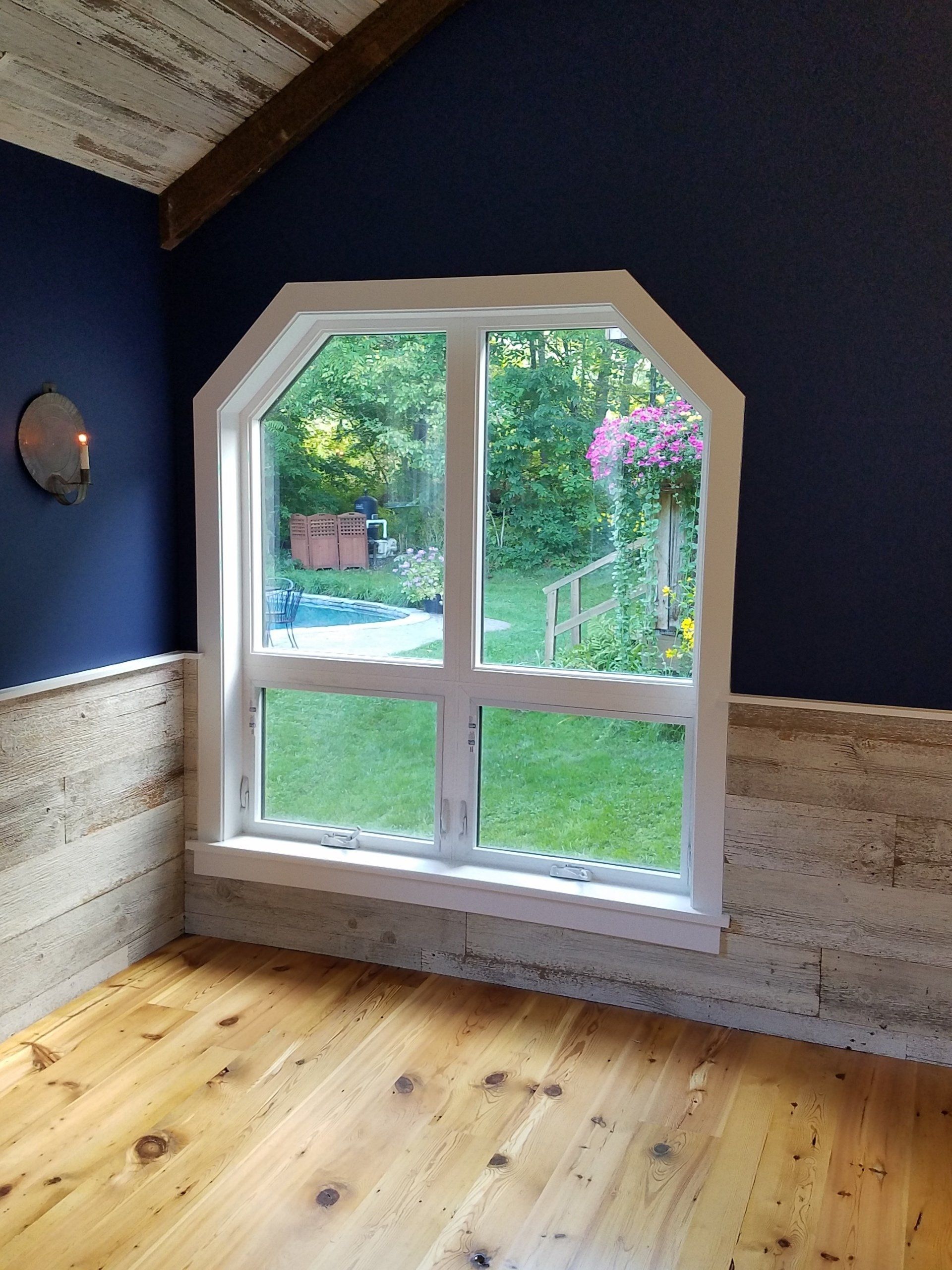 Window with a white frame overlooking a backyard. Dark blue walls and wood siding surround.