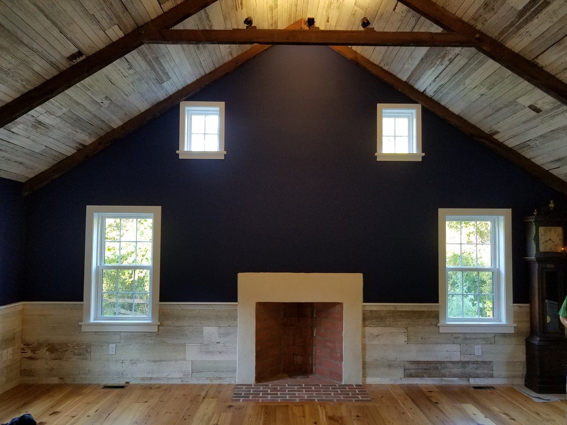 Interior of room with dark blue wall, fireplace, windows, and wood ceiling/flooring.