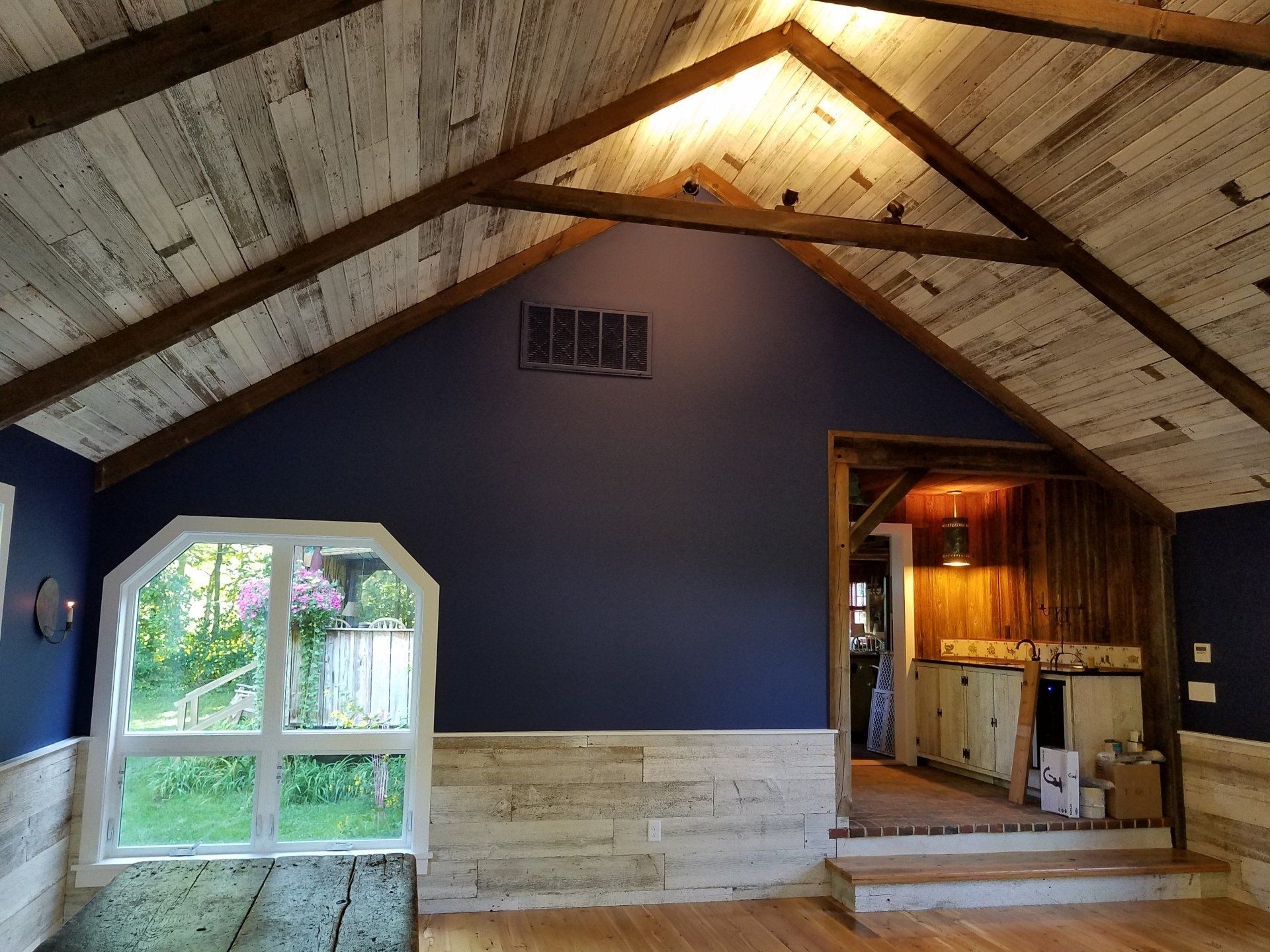 Interior of a room with blue walls, wood beams, and a window overlooking greenery.