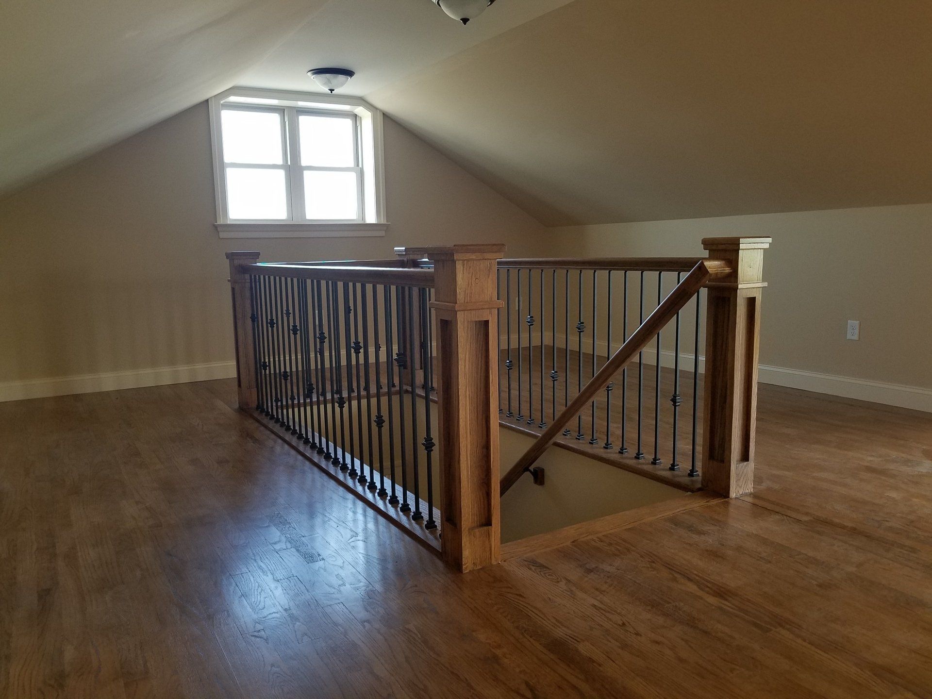 Loft with wooden floor and railing, arched ceiling, and small window.