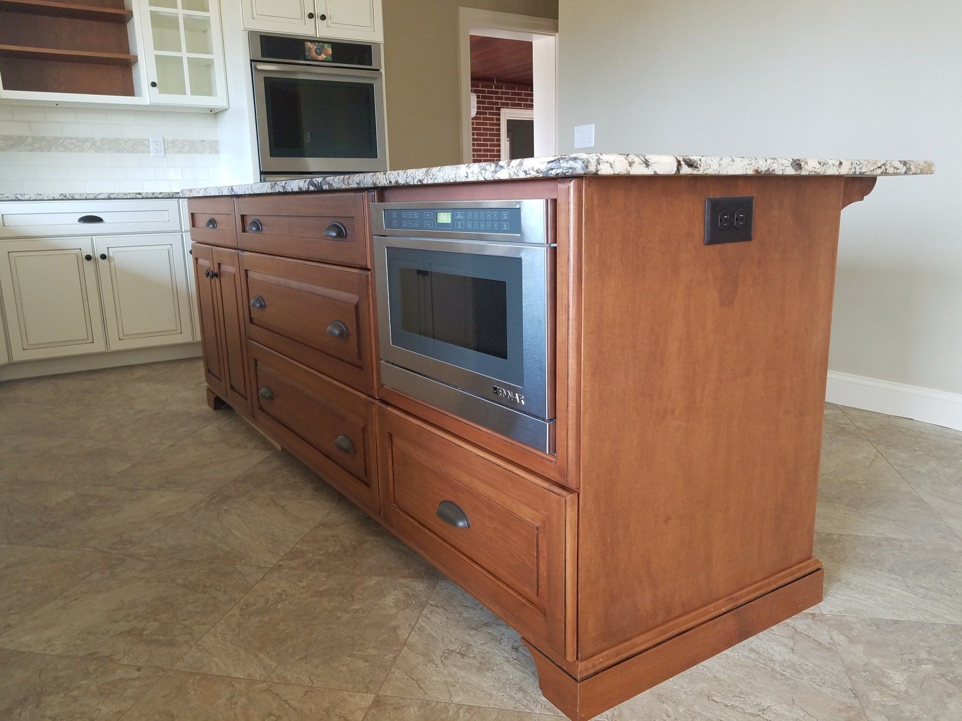 Kitchen island with built-in microwave, drawers, and granite countertop; wooden cabinets.