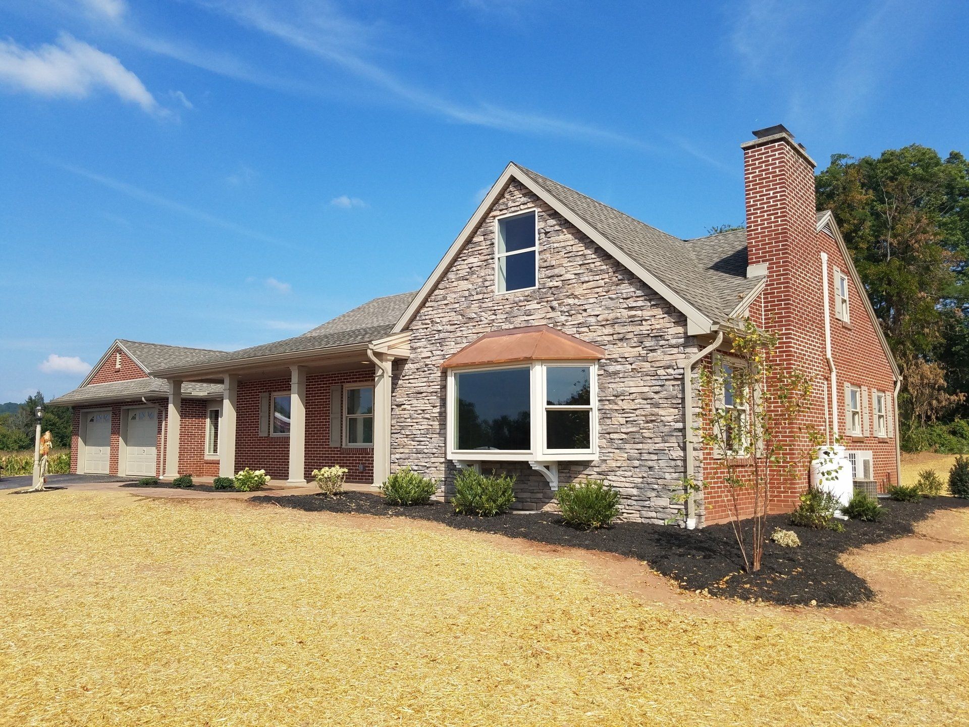 House exterior with stone and brick facade, arched window, chimney, and blue sky.