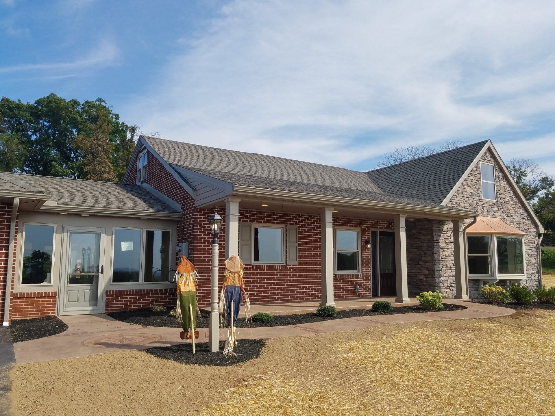 A brick and stone house with a porch and multiple windows under a blue sky.