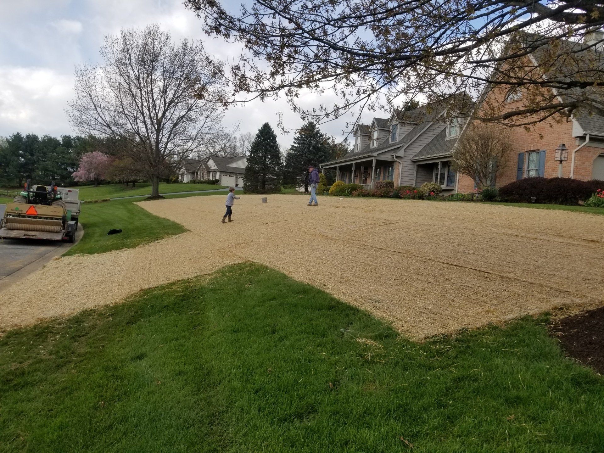 Large residential yard with gravel, grass, and two people playing. A trailer sits in the background.