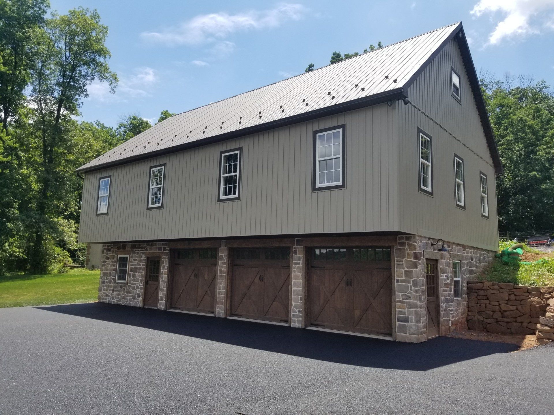 Two-story building with three garage doors. Stone base supports olive-green siding and metal roof.