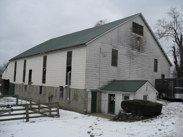 White barn with green roof, small attached shed, and snow on the ground.