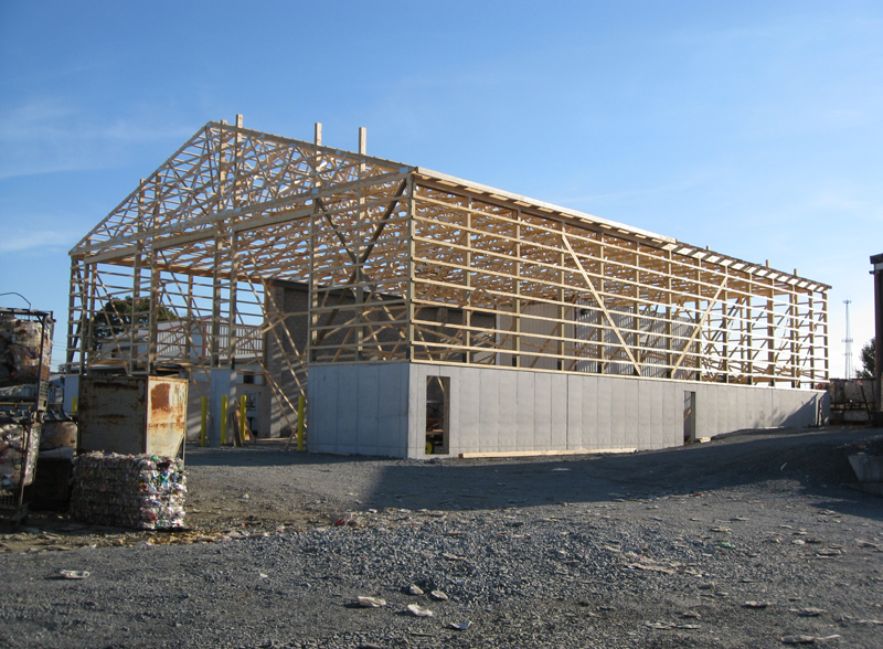 Wooden building under construction, with gray concrete walls, against a blue sky.