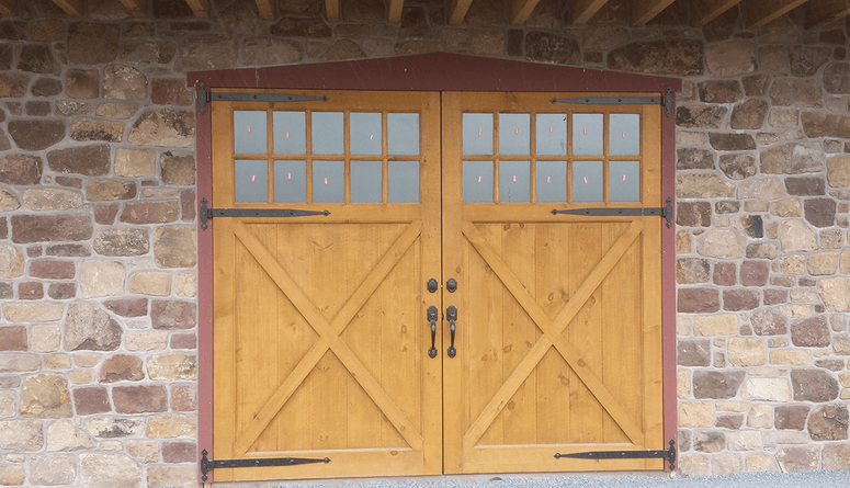 Wooden double doors with glass panels and black hardware set in a stone wall.
