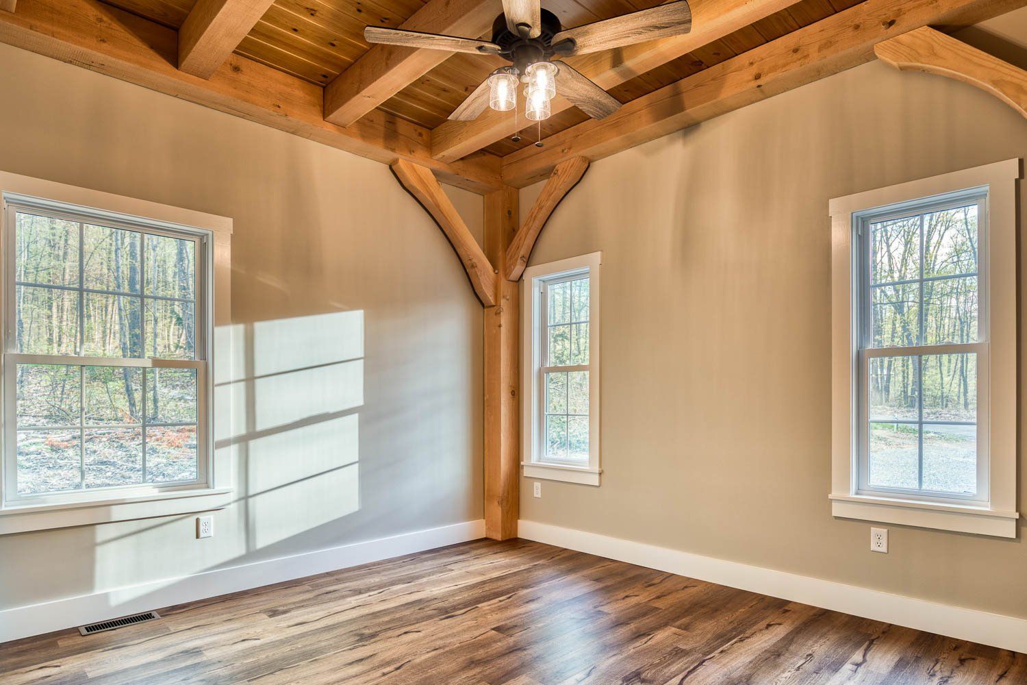 Room with wooden beams, three windows, and hardwood floors. Beige walls, natural light.