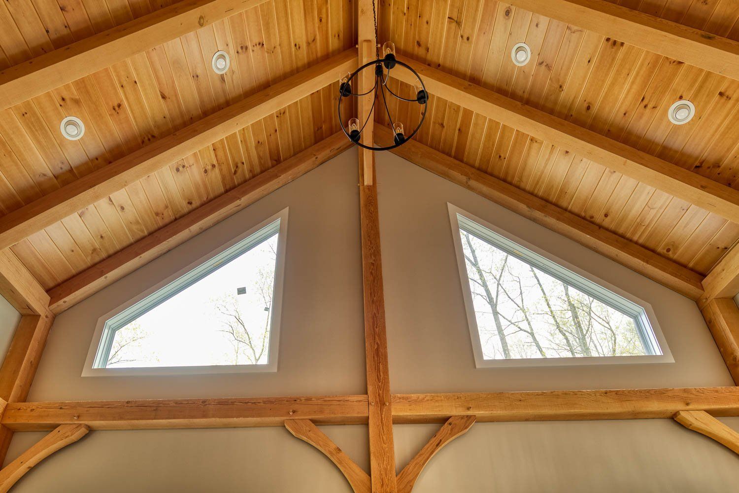 Wood-beamed ceiling with two triangular windows, a chandelier, and neutral walls.