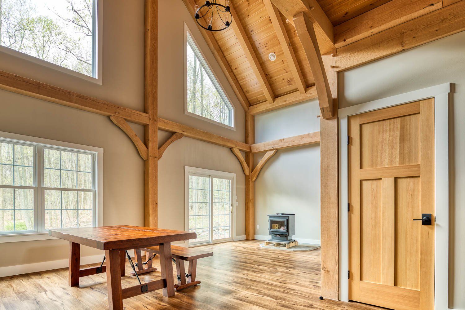 Interior of a home with exposed wooden beams, a table, and windows overlooking trees.