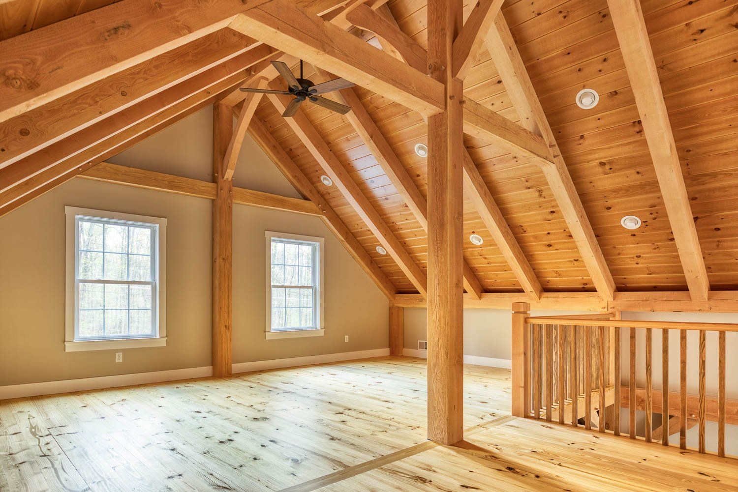 Wooden attic space with exposed beams, two windows, and a railing.